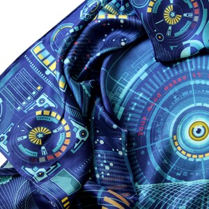 Puede incluir: Bufanda azul oscuro con un dise&ntilde;o futurista con patrones de circuitos y gr&aacute;ficos circulares en tonos turquesa, amarillo y naranja. El texto "Your mind makes it real" es visible. La bufanda est&aacute; doblada y drapeada.