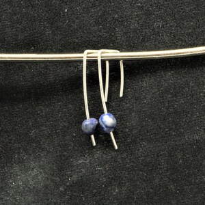 Op de afbeelding: Een paar zilveren oorbellen met blauwe lapis lazuli stenen die aan een zilveren staaf hangen.