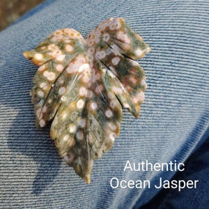 May include: Hand-carved, realistic maple leaf made of authentic Ocean Jasper. The leaf features a detailed design with green, white, and pink hues. The image includes the text "Hand Carved Realistic Maple Leaf" and "Authentic Ocean Jasper".
