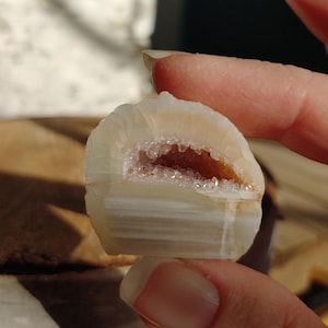 May include: A small, polished geode half, showcasing layers of creamy white and tan hues. The interior reveals a sparkling crystal-lined cavity with a warm, amber color. A natural, decorative stone.