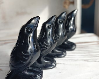 May include: Four small, polished black bird figurines carved from stone, arranged in a single file line. Each bird features a smooth, glossy surface, a pointed beak, and etched wing details, standing upright on a flat base in a uniform, side-facing pose.