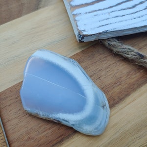 Blue chalcedony natural crystal slice. Small blue and white stone. Meditation stone pictured on butcher block wood table, next to vintage wood ruler. Shaded light, cool blue undertones.