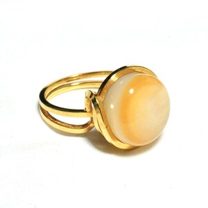 May include: A gold ring with a large, round, white and yellow gemstone.