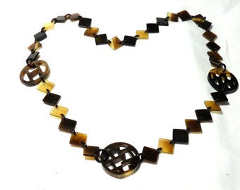 Peut inclure: Un collier brun et noir composé de pièces carrées et rondes en corne. Les pièces rondes sont sculptées.