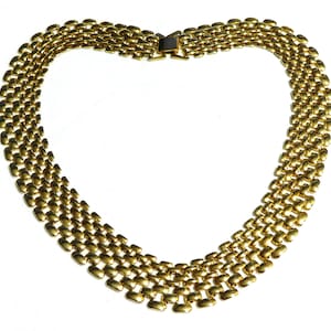 May include: A gold-coloured necklace featuring a woven design. The necklace is made up of multiple rows of rectangular links, giving it a textured look. The clasp is visible at the top, and the necklace is set against a white background.