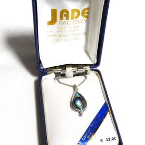 May include: A silver-toned pendant necklace with an abalone shell inlay, presented in a blue box. The box is labeled "JADE FACTORY" and "Genuine Paua Shell Sterling Silver". The necklace features a teardrop-shaped pendant.