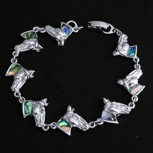 May include: A silver bracelet with a chain link design features eight horse head charms. Each charm is adorned with iridescent abalone shell inlay.