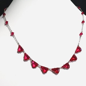 May include: A silver-toned necklace featuring a series of vibrant red, triangular-shaped faceted crystals suspended along a delicate metal chain, accented with smaller red crystal beads interspersed throughout the length of the jewelry piece.