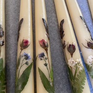May include: Five ivory taper candles with pressed flowers and greenery. The flowers include lavender, forget-me-nots, and roses.