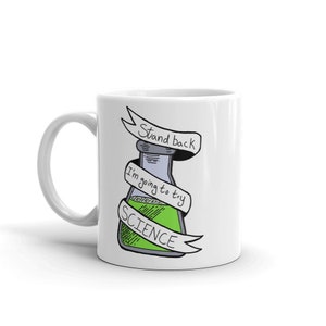 May include: White ceramic mug featuring a green and grey cartoon beaker with the text "Stand back I'm going to try SCIENCE" on a white ribbon.