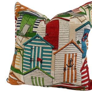 May include: A colorful throw pillow with a beach hut pattern. The pillow features a variety of colors, including red, blue, green, yellow, and orange. The beach huts are depicted in a whimsical style, with striped doors and windows.