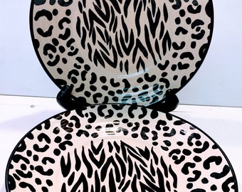 May include: Two ceramic plates with a black and white animal print design. The plates feature a zebra stripe pattern and leopard spots.