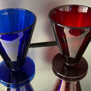 Puede incluir: Dos vasos de vidrio con base acampanada. Un vaso es azul cobalto y el otro es rojo rubí.