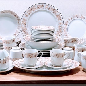 May include: A set of white porcelain dinnerware with a brown floral pattern. The set includes dinner plates, salad plates, bowls, cups, saucers, a creamer, and a sugar bowl.