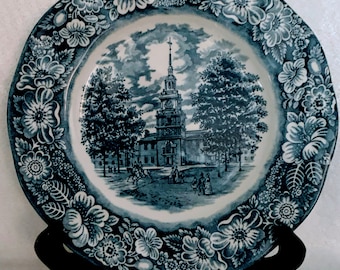 Könnte beinhalten: Blau-weiße Keramikplatte mit floralem Rand und einer Szene mit einem historischen Gebäude in der Mitte. Das Gebäude ist von Bäumen umgeben und hat einen Uhrturm.