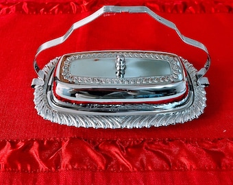May include: A silver butter dish with a glass lid and a decorative handle. The dish has a rope-like design around the edge.