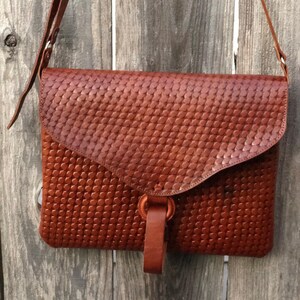 Peut inclure: Un sac &agrave; bandouli&egrave;re en cuir marron avec un motif tiss&eacute;. Le sac a une fermeture &agrave; rabat et une longue bandouli&egrave;re.