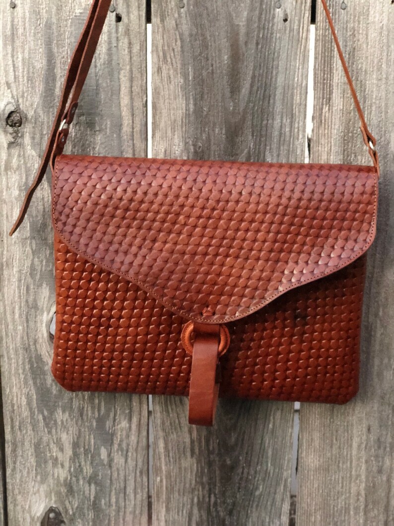 Peut inclure: Un sac &agrave; bandouli&egrave;re en cuir marron avec un motif tiss&eacute;. Le sac a une fermeture &agrave; rabat et une longue bandouli&egrave;re.