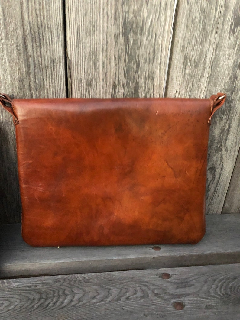 Peut inclure: Un sac messager en cuir brun avec une fermeture &agrave; rabat et une bandouli&egrave;re. Le sac est fait de cuir souple et doux et a un aspect vintage.