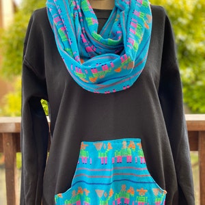 May include: Black sweatshirt with a blue and green patterned pocket and a matching blue and green patterned infinity scarf.