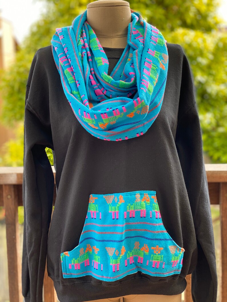 May include: Black sweatshirt with a blue and green patterned pocket and a matching blue and green patterned infinity scarf.