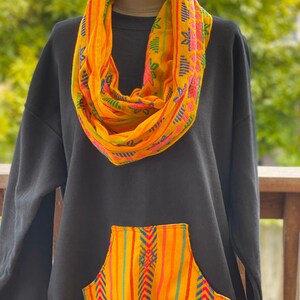 May include: Black sweatshirt with a yellow and blue patterned pocket and a matching yellow and blue patterned scarf.