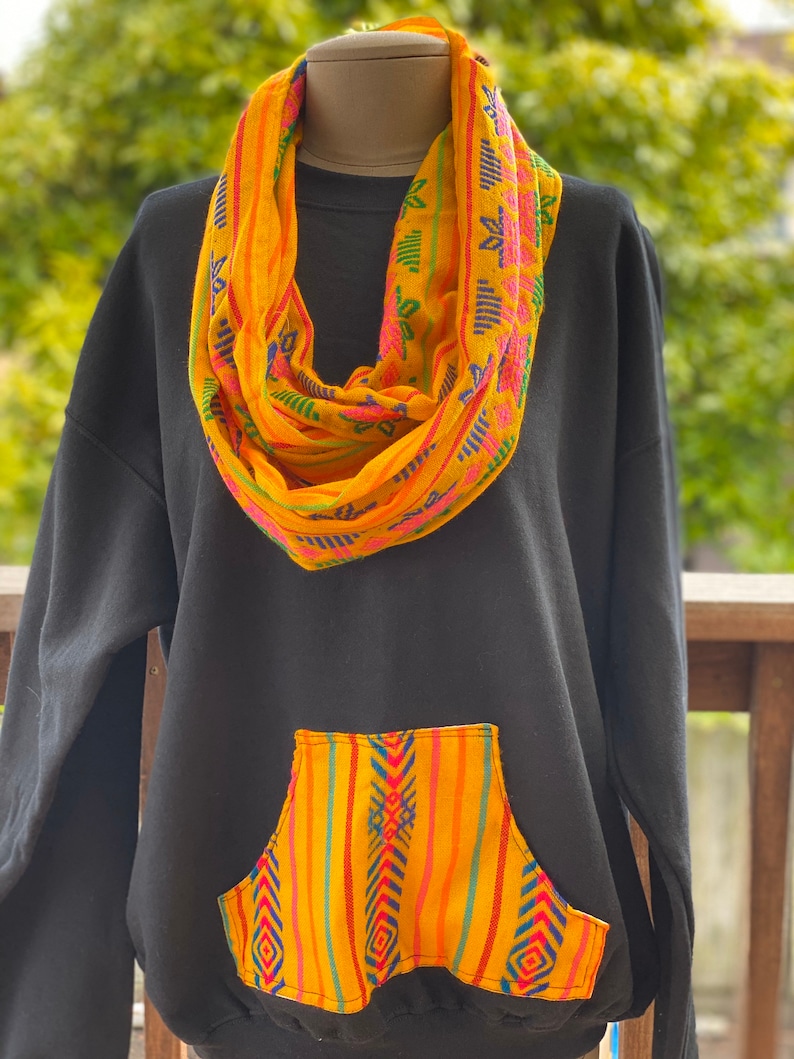 May include: Black sweatshirt with a yellow and blue patterned pocket and a matching yellow and blue patterned scarf.