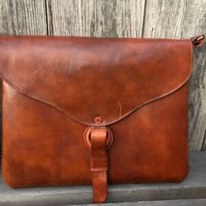 Peut inclure: Un sac &agrave; main en cuir marron avec une fermeture &agrave; rabat et une longue bandouli&egrave;re. Le sac a un aspect us&eacute; et vintage.