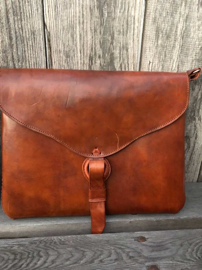 Peut inclure: Un sac &agrave; main en cuir marron avec une fermeture &agrave; rabat et une longue bandouli&egrave;re. Le sac a un aspect us&eacute; et vintage.