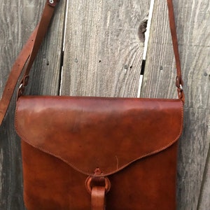 Peut inclure: Un sac &agrave; bandouli&egrave;re en cuir marron avec une fermeture &agrave; rabat et une sangle &agrave; boucle. Le sac a une seule bandouli&egrave;re et une poign&eacute;e nou&eacute;e.