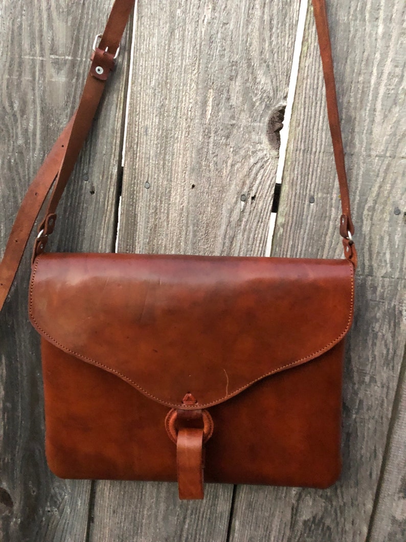 Peut inclure: Un sac &agrave; bandouli&egrave;re en cuir marron avec une fermeture &agrave; rabat et une sangle &agrave; boucle. Le sac a une seule bandouli&egrave;re et une poign&eacute;e nou&eacute;e.