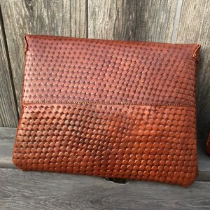 Peut inclure: Une pochette en cuir marron avec un motif tiss&eacute;. La pochette a une fermeture &agrave; rabat et une couture sur le devant.