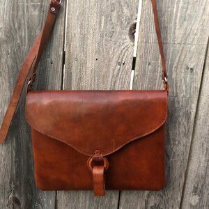 Peut inclure: Un sac &agrave; bandouli&egrave;re en cuir marron avec une fermeture &agrave; rabat et une boucle. Le sac a une longue bandouli&egrave;re pour le porter &agrave; l'&eacute;paule.