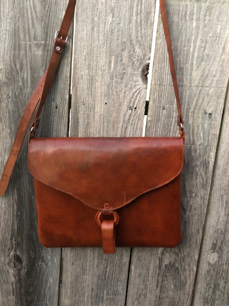Peut inclure: Un sac &agrave; bandouli&egrave;re en cuir marron avec une fermeture &agrave; rabat et une boucle. Le sac a une longue bandouli&egrave;re pour le porter &agrave; l'&eacute;paule.