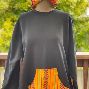 May include: Black sweatshirt with a large pocket on the front. The pocket is made of colorful fabric with a geometric pattern in yellow, orange, red, blue, and green.