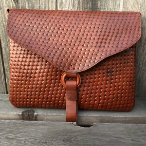 Peut inclure: Une pochette d'enveloppe en cuir marron avec un motif tiss&eacute; et une sangle en cuir avec une boucle en m&eacute;tal.