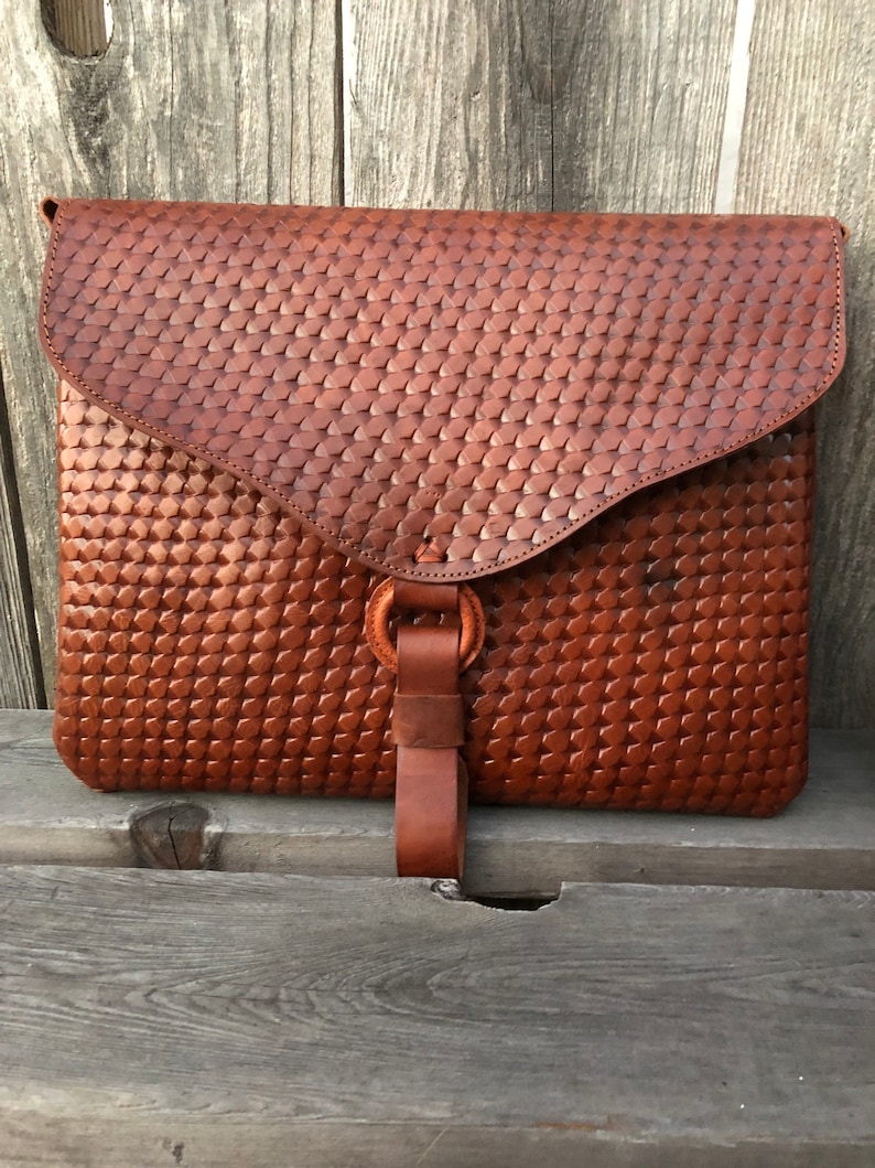 Peut inclure: Une pochette d'enveloppe en cuir marron avec un motif tiss&eacute; et une sangle en cuir avec une boucle en m&eacute;tal.