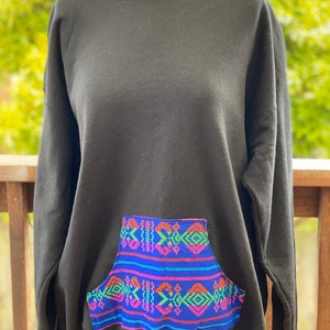 May include: Black sweatshirt with a large front pocket featuring a colorful geometric pattern in shades of blue, green, pink, and orange.