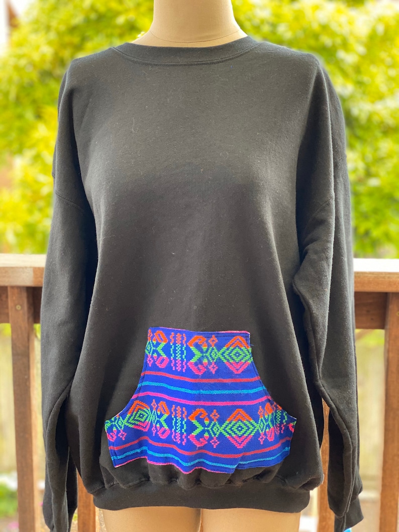 May include: Black sweatshirt with a large front pocket featuring a colorful geometric pattern in shades of blue, green, pink, and orange.