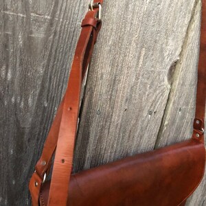 Peut inclure: Un sac &agrave; main en cuir marron avec une longue bandouli&egrave;re r&eacute;glable. Le sac a une fermeture &agrave; rabat et une boucle argent&eacute;e.