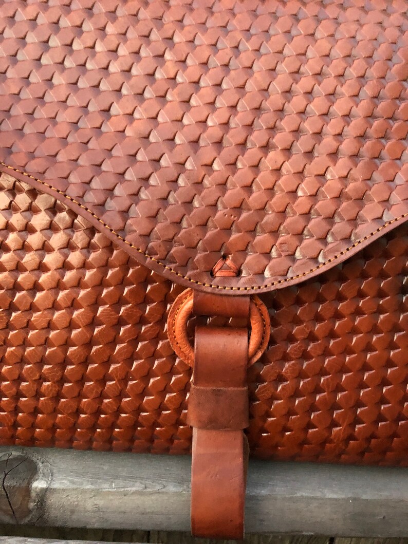 Peut inclure: Un sac en cuir brun avec un motif tiss&eacute; et une sangle en cuir avec un anneau m&eacute;tallique.