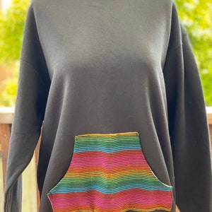 May include: Black sweatshirt with a rainbow striped pocket. The pocket is sewn on with a gold thread.