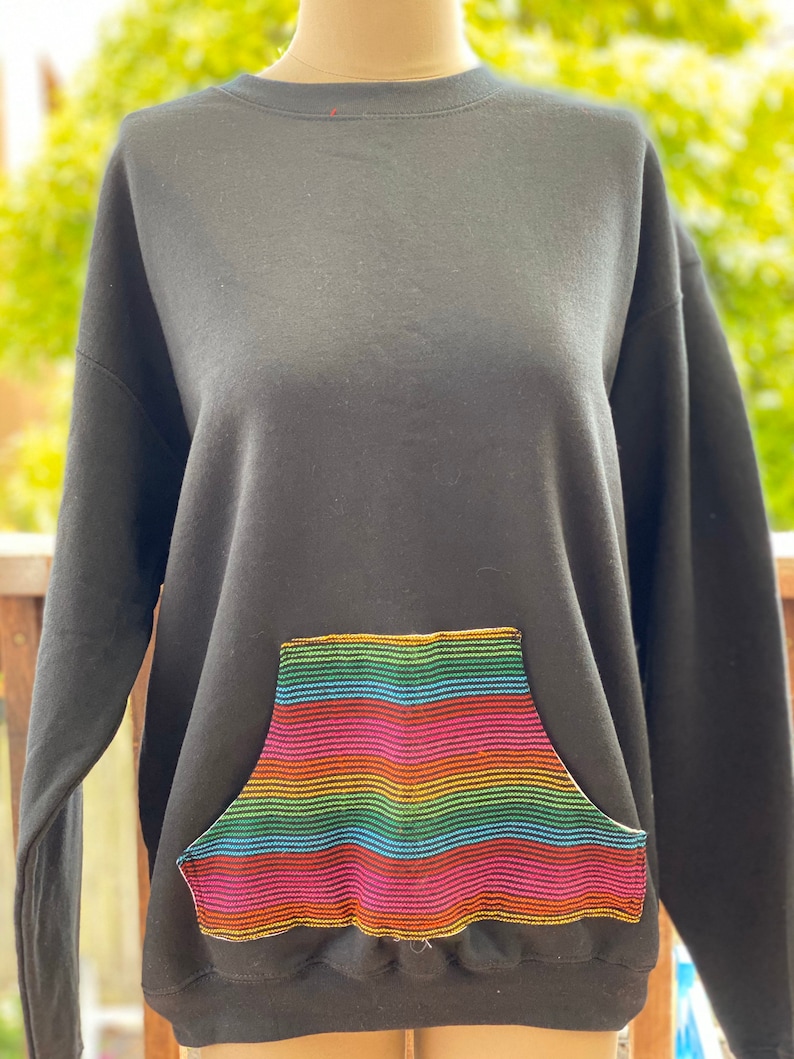 May include: Black sweatshirt with a rainbow striped pocket. The pocket is sewn on with a gold thread.