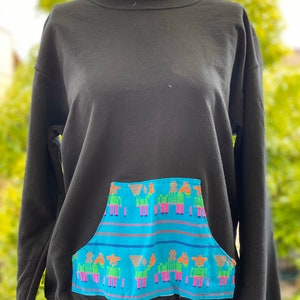 May include: Black sweatshirt with a blue and multi-colored pocket featuring a repeating pattern of stylized figures.