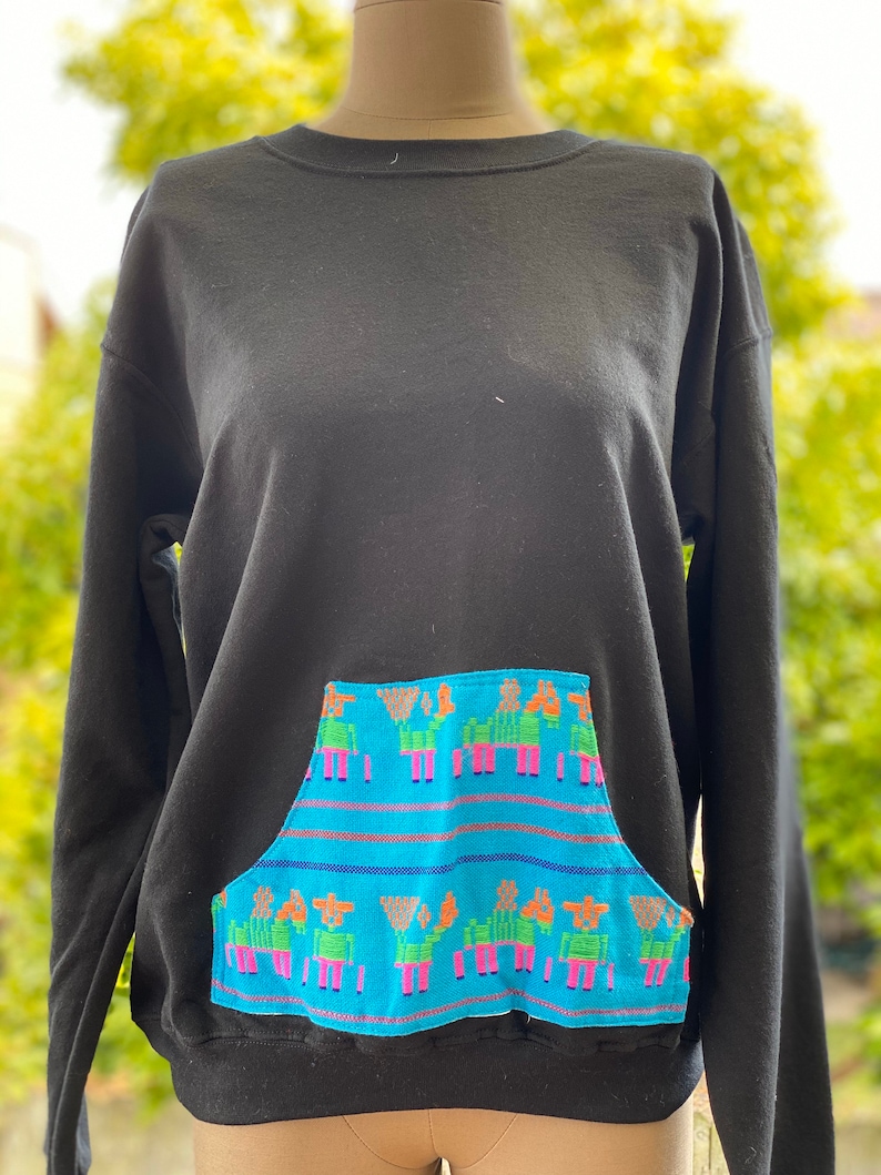 May include: Black sweatshirt with a blue and multi-colored pocket featuring a repeating pattern of stylized figures.