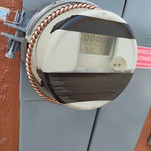 May include: A close-up of a white electric meter with a black face and a copper wire wrapped around it. The meter reads "8888".
