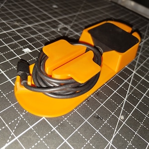 May include: Orange plastic headphone holder with a black base and a black cord wrapped around it.