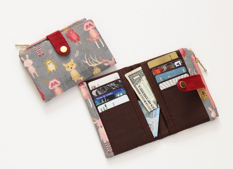 May include: Two fabric wallets, one with a gray background and a colorful animal print, and the other with a brown interior and a pink and gray animal print. Both wallets have a zipper closure and a red button.
