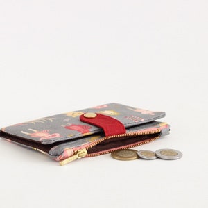 May include: A gray wallet with a floral print and a red flap closure. The wallet is open and has a zippered compartment with coins inside.
