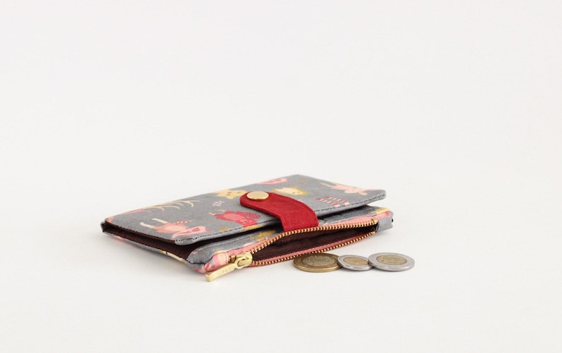 May include: A gray wallet with a floral print and a red flap closure. The wallet is open and has a zippered compartment with coins inside.